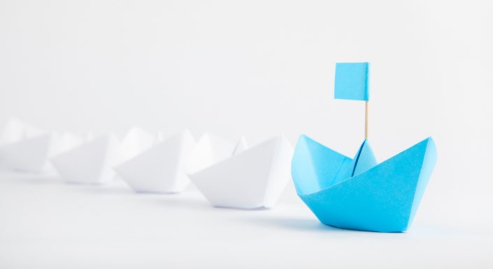Leadership concept with blue paper ship leading among white